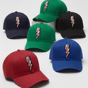 Könnte beinhalten: Eine Auswahl an Baseballkappen in verschiedenen Farben, darunter Rot, Grün, Blau, Schwarz und Marineblau. Jede Kappe zeigt ein Blitzdesign mit einem Baseball-Nahtmuster. Die Kappen sind vor einem weißen Hintergrund angeordnet.