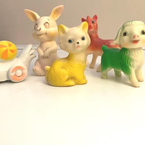 May include: A collection of vintage rubber animal toys. The toys include a white duck on wheels, a standing bunny, a yellow cat, a red deer, and a green and white pig. The toys are in various colors and have a retro aesthetic.