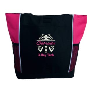May include: Black tote bag with pink accents and white mesh side pockets. The bag has an embroidered design of a ribcage with the name "Gabriella" and the text "X-Ray Tech".