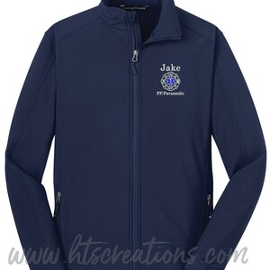 May include: Navy blue soft-shell jacket with a zipper closure. The jacket has a white embroidered name "Jake" and a firefighter/paramedic logo with the text "FF/Paramedic".
