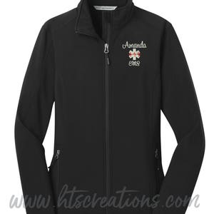 May include: Black softshell jacket with a zipper closure and two pockets. The jacket has a white embroidered design with the text "Amanda EMS" and a red medical symbol.