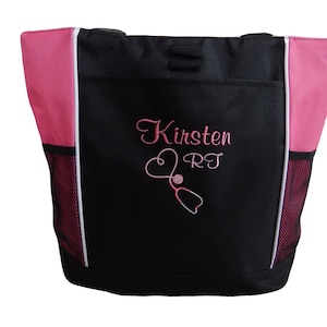 May include: Black tote bag with pink accents and a white zipper. The bag has a mesh pocket on the side and is embroidered with the name "Kirsten RT" and a pink stethoscope.