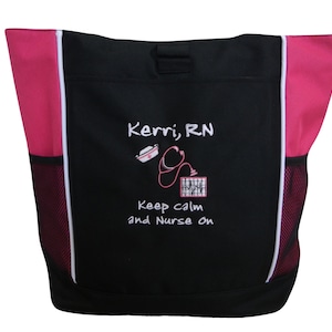May include: Black tote bag with pink accents and white trim. The bag has a mesh pocket on each side. The front of the bag features white embroidery that says "Kerri, RN" with a nurse's cap, stethoscope, and EKG reading. The text below the image says "Keep calm and Nurse on."