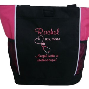 May include: Black tote bag with pink accents and white piping. The bag has a mesh pocket on the side and features embroidered text that reads "Rachel RN, BSN Angel with a stethoscope!"