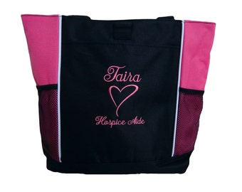 May include: Black tote bag with pink accents and white piping. The bag has a mesh pocket on each side. The front of the bag is embroidered with the name "Taira" in pink cursive lettering, a pink heart, and the words "Hospice Aide" in pink cursive lettering.