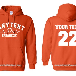 May include: Orange hooded sweatshirt with a white heartbeat graphic and the text "ANY TEXT PARAMEDIC" on the front. The back of the sweatshirt has the text "YOUR TEXT 22" in white.