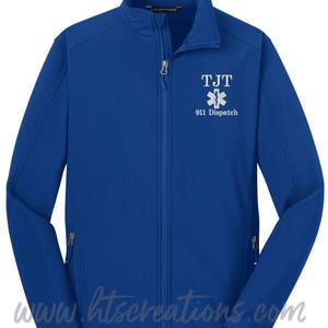May include: A royal blue soft-shell jacket with a zipper closure. The jacket has a white embroidered logo with the text "TJT 911 Dispatch" and a stylized medical symbol.