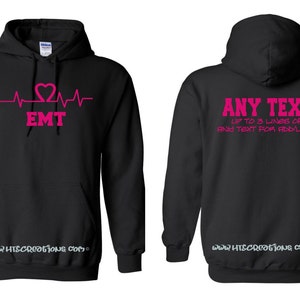 May include: Black hooded sweatshirt with a pink heart beat graphic and the text "EMT". The back of the sweatshirt has the text "ANY TEXT UP TO 3 LINES OF FINE TEXT FOR ADD'L £10".