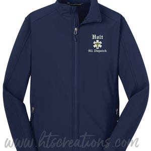 May include: Navy blue zip-up jacket with the text "Holt 911 Dispatch" embroidered on the chest. The jacket has a stand-up collar, two zippered pockets, and the website www.htscreations.com printed at the bottom.