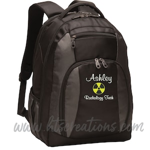 May include: Black and gray backpack with a zippered pocket and a white embroidered name "Ashley" and the text "Radiology Tech" with a yellow and black radiation symbol.