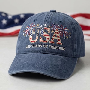 May include: A blue denim baseball cap with the word "USA" embroidered in red, white, and blue, with fireworks and stars. The text "250 YEARS OF FREEDOM" is below the word "USA".