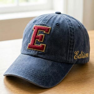 May include: A blue denim baseball cap with a red and gold embroidered "E" on the front. The word "Edison" is embroidered in gold script on the side of the cap.
