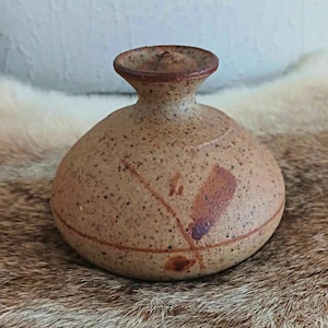 Könnte beinhalten: Kleine, gesprenkelte, braune Keramikvase mit rundem Körper und schmalem Hals. Die Vase hat einen dunkelbraunen Rand und ist mit einem einfachen, abstrakten Design in Braun- und Marontönen verziert. Die Vase ist etwa 10 cm hoch.