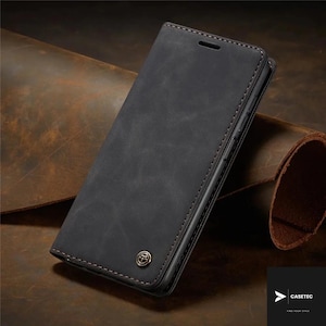 May include: A black leather phone case with a magnetic closure. The case has a distressed finish and brown stitching around the edges. A small, gold-colored emblem is visible on the front. The brand name "CASETEC" is in the bottom right corner.