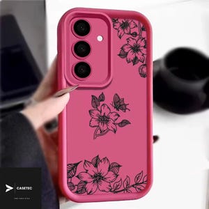May include: A vibrant pink phone case adorned with a floral pattern. The case showcases black outlines of flowers and a butterfly. It has a raised edge around the camera and a logo in the bottom left corner.