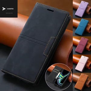 Könnte beinhalten: Schwarze Leder-Handyhülle mit Magnetverschluss und Kartenfächern. Die Hülle hat einen genähten Rand und eine strukturierte Oberfläche. Das Bild zeigt auch mehrere andere Farboptionen, darunter Lila, Blau, Burgunder, Rosa und Braun.