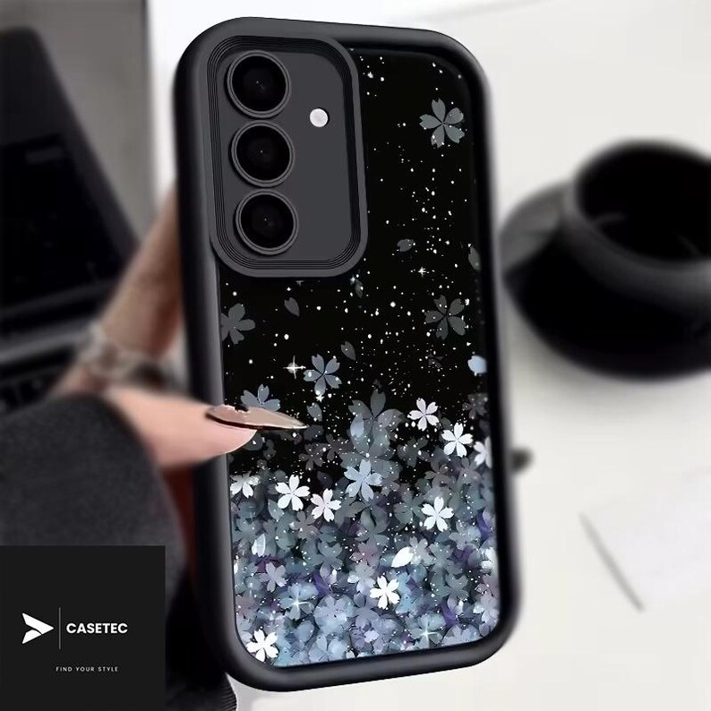 May include: Black phone case with a floral design. The case features a black border and a black background with white and blue flowers. The brand name "CASETEC" is visible in the bottom left corner.