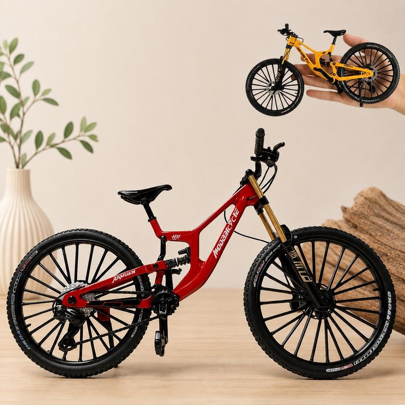 May include: A miniature red mountain bike model with black wheels, a black seat, and gold-toned front suspension forks. The frame features white text detailing. A second, smaller yellow mountain bike model is shown held in the upper right corner.