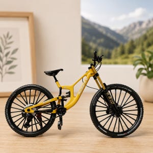 May include: A yellow mountain bike model with black wheels, a black seat, and black handlebars. The frame features the text "MCEBICYCLE" in white lettering. The bike has a rear suspension system, a chain, and black spokes on both wheels.