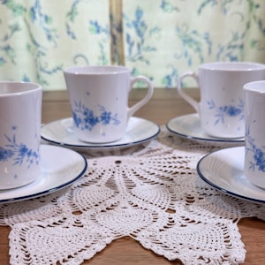 Puede incluir: Un juego de cuatro tazas y platillos de cerámica blanca, cada uno con un delicado patrón floral azul. Los platillos tienen un borde azul fino y las tazas cuentan con un asa curva. El diseño es consistente en todas las piezas del conjunto.
