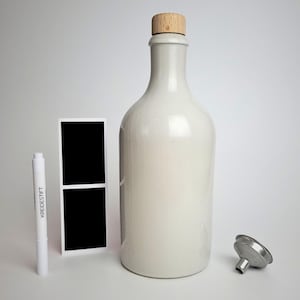 Könnte beinhalten: Eine cremefarbene Keramikflasche mit einem Holzstopfen, einem kleinen Metalltrichter, einem weißen Marker mit dem Text "KREIDESTIFT" und einem schwarzen rechteckigen Etikett mit weißem Rand. Die Flasche hat eine abgerundete Form.