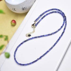 Peut inclure: Un collier délicat composé de petites pierres bleues carrées. Le collier, doté d'un fermoir doré, est présenté sur une surface blanche. Les pierres précieuses sont d'un bleu profond, suggérant un bijou de haute qualité.