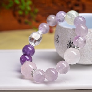 Könnte beinhalten: Ein Armband mit einer Mischung aus lila, lavendelfarbenen und rosa Edelsteinen. Das Armband enthält eine klare, facettierte Perle und kleine silberfarbene Abstandshalter. Die Edelsteine variieren in Größe und Form.