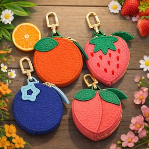 May include: Four fruit-shaped coin purses with gold-tone hardware. The purses are designed as an orange, strawberry, blueberry, and peach. Each has a zipper closure and a green leaf accent. The orange is bright orange, the strawberry is pink, the blueberry is blue, and the peach is coral.