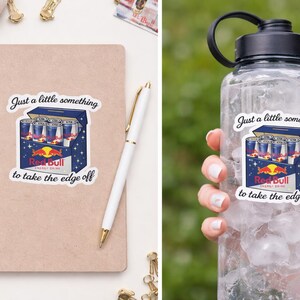 May include: A sticker showing a cartoon Red Bull energy drink carton with the text "Just a little something to take the edge off." The sticker is on a notebook and a water bottle.