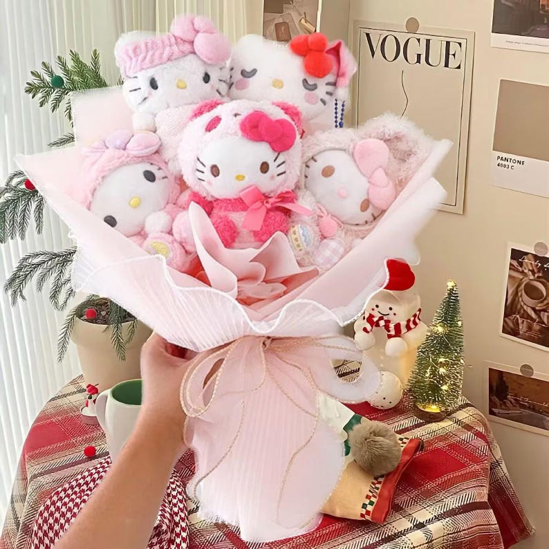 May include: A bouquet of plush Hello Kitty dolls in various pink outfits, wrapped in pink tissue paper and tied with a pink ribbon. The dolls have bows and headbands. The background includes a Vogue magazine cover and a small Christmas tree.