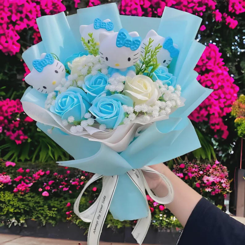 May include: A bouquet of blue and white roses and white baby's breath, wrapped in light blue paper. The bouquet includes several Hello Kitty figures with blue bows. A white ribbon with the text "Always By Your Side" is tied around the base.