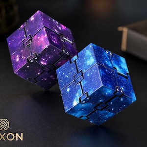 Puede incluir: Dos juguetes antiestrés con forma de cubo con diseño de galaxia. Uno es morado, el otro azul, ambos con detalles blancos en forma de estrella. Los juguetes están conectados por bisagras, lo que permite manipularlos. La marca "TEXON" es visible.