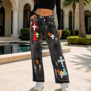 May include: Black long-sleeve crop top paired with charcoal gray denim jeans featuring a distressed wash and a scattered pattern of colorful cross-shaped patches in red, yellow, orange, white, and light blue, finished with a raw frayed hem.
