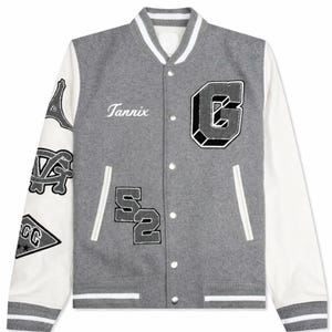 May include: Gray varsity jacket with white sleeves and trim. Features the name "Tannix" in script, a large "G" patch, and other patches on the sleeves. The jacket has a button-up front.