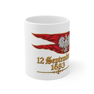 Peut inclure: Un mug en céramique blanche orné d'un drapeau rouge à deux pointes portant un emblème d'aigle blanc couronné. Sous le drapeau, le texte 12 September 1683 est imprimé en police gothique dorée, souligné par une ligne dorée avec une croix.