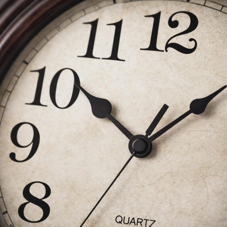 May include: Close-up of a vintage-style clock face. The clock features large black numerals against a cream-colored background with a distressed texture. The black hands point to approximately 10:58. The word "QUARTZ" is printed at the bottom.