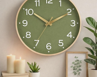 May include: A round wall clock with a green face and white numerals. The clock has gold-colored hands and a light wood frame. The clock is surrounded by candles, plants, and a framed botanical print, creating a cozy, decorative scene.