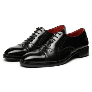 May include: A pair of black oxford shoes featuring a glossy finish, decorative brogue detailing along the cap toe and side panels, black laces, and a vibrant red interior lining. The shoes have a low heel and a structured, polished appearance.