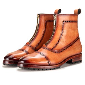 May include: A pair of brown leather ankle boots with a front zipper closure and decorative perforations. The boots have a cap toe design and a small heel. The leather has a polished finish.
