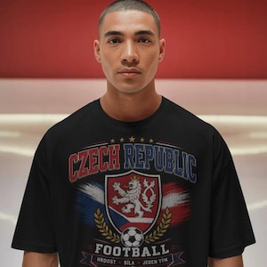 Può includere: T-shirt nera con la scritta "CZECH REPUBLIC FOOTBALL" e uno stemma con i colori della Repubblica Ceca e un pallone da calcio. Il design include pennellate rosse, bianche e blu.