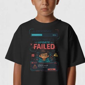 Op de afbeelding: Zwart t-shirt met een afbeelding van een persoon en de tekst "UPDATE FAILED". Het ontwerp bevat een laadbalk en de woorden "LOADING" en "PERSONALITY". Het t-shirt wordt door een persoon gedragen.