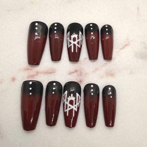 May include: A set of ten press-on nails featuring a glossy ombre finish that transitions from black at the tips to a deep dark red at the base. Several nails are accented with small white dots, while the middle nails feature a white line art design.