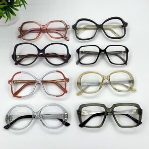 Könnte beinhalten: Acht Brillenpaare, angeordnet in zwei Spalten. Die Gestelle haben verschiedene Farben, darunter durchscheinendes Rosa, Schwarz, Dunkelblau, Transparent, rot-weiß gestreift, Beige und Olivgrün, alle mit markanten runden oder eckigen Formen.