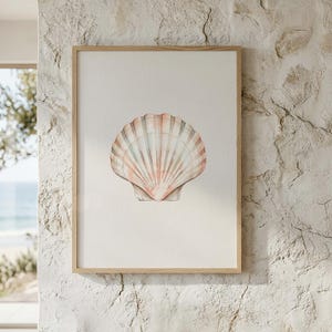 May include: A framed wall art print featuring a centered illustration of a single scallop shell. The shell displays soft, muted tones of peach, pink, and light grey with distinct vertical ridges. The artwork is enclosed in a light-colored wooden frame.