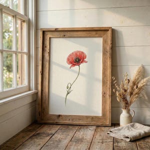 Könnte beinhalten: Ein gerahmter Aquarelldruck einer roten Mohnblume. Das Kunstwerk ist in einem rustikalen, hellbraunen Holzrahmen gefasst. Der Mohn hat einen grünen Stiel und ist vor einem cremefarbenen Hintergrund platziert. Der Rahmen wird auf einer Holzoberfläche ausgestellt.