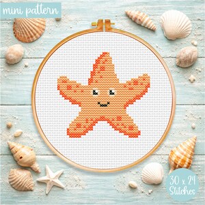 May include: A cross-stitch pattern of a smiling starfish in an embroidery hoop. The starfish is orange with black details. The background includes seashells and sand on a light blue wooden surface. The text "mini pattern" and "30 x 24 stitches" are visible.