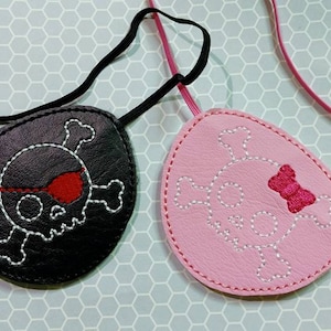 May include: Two skull and crossbones eye patches, one black with a red eye patch and one pink with a pink bow. Both have white stitching.