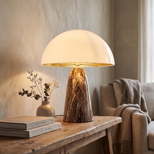 May include: A table lamp featuring a smooth, white, dome-shaped shade and a conical base made of brown marble with white veining. The lamp emits a warm glow, illuminating the interior of the shade, which has a metallic gold-toned finish.