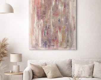 May include: Abstract art canvas with vertical brushstrokes in shades of pink, purple, and beige. The artwork hangs above a cream-colored sofa with neutral-toned throw pillows. A round wooden coffee table and a side table with a lamp complete the living room setting.