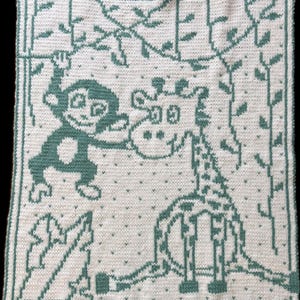 May include: A knitted baby blanket featuring a monkey and giraffe in a jungle scene. The design is in teal on a white background. The monkey is hanging from a vine, and the giraffe is standing. The blanket is square.
